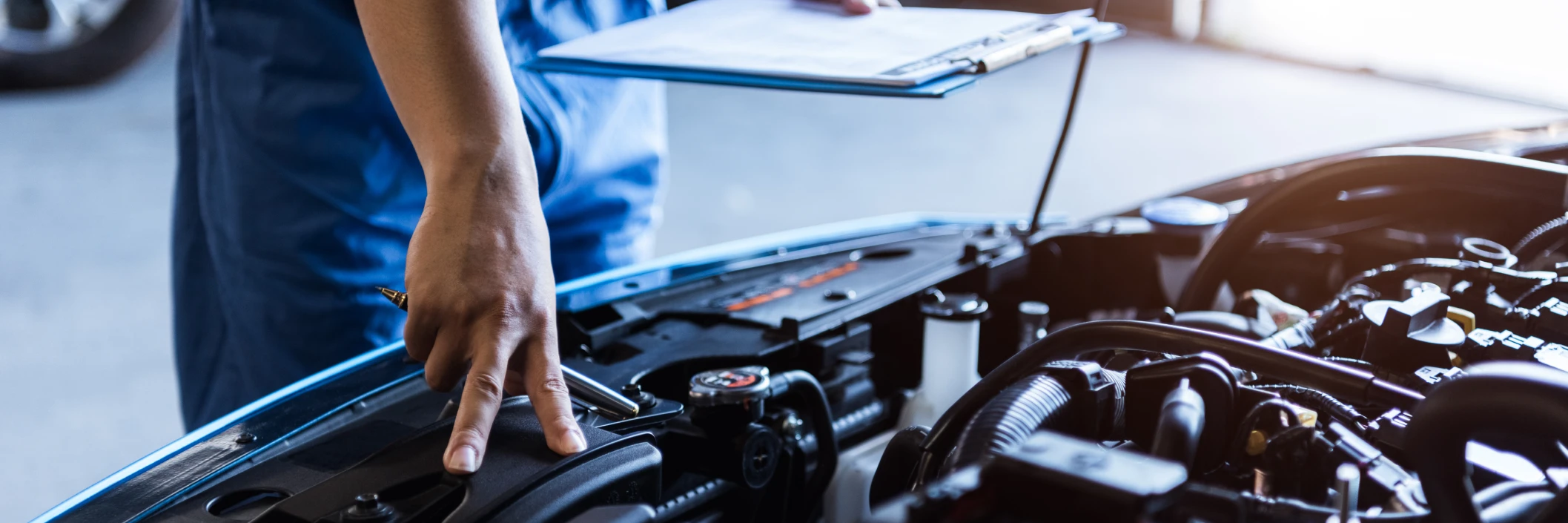 A mechanic in blue overalls inspects a car engine while holding a clipboard. The scene conveys attention to detail and professionalism in an auto repair shop.