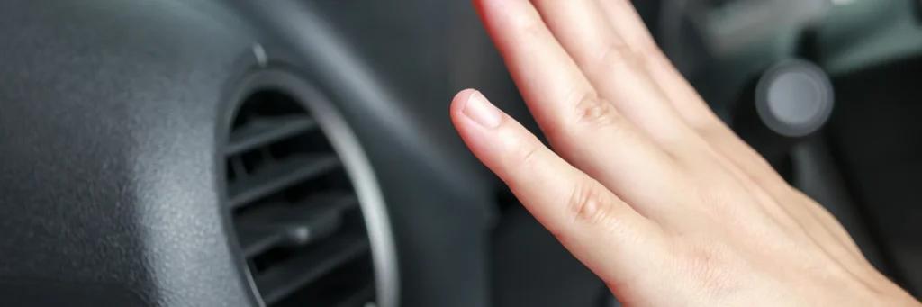 A hand is held up to feel the air from a car vent inside a vehicle, conveying a sense of checking temperature or air flow. The scene is calm and focused.