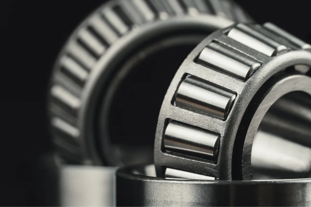 Close-up of two metallic roller bearings with shiny surfaces, stacked against a dark background. The image conveys industrial precision and strength.