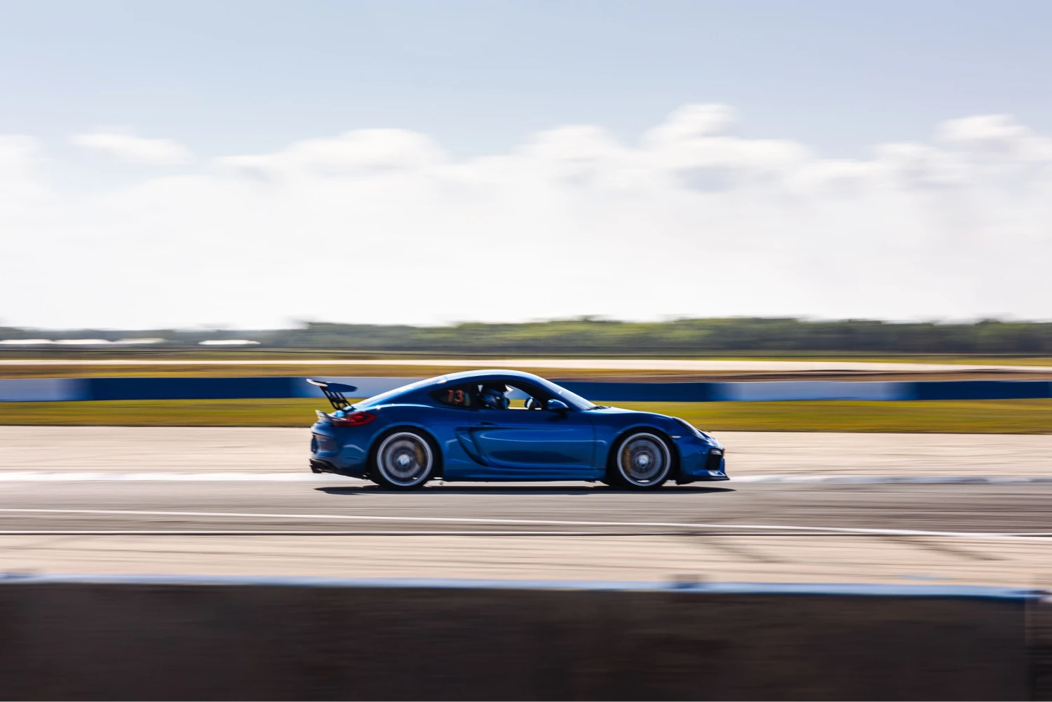 A blue sports car speeds along a racetrack under a clear sky. Motion blur conveys speed, while the background of grassy fields adds depth and contrast.