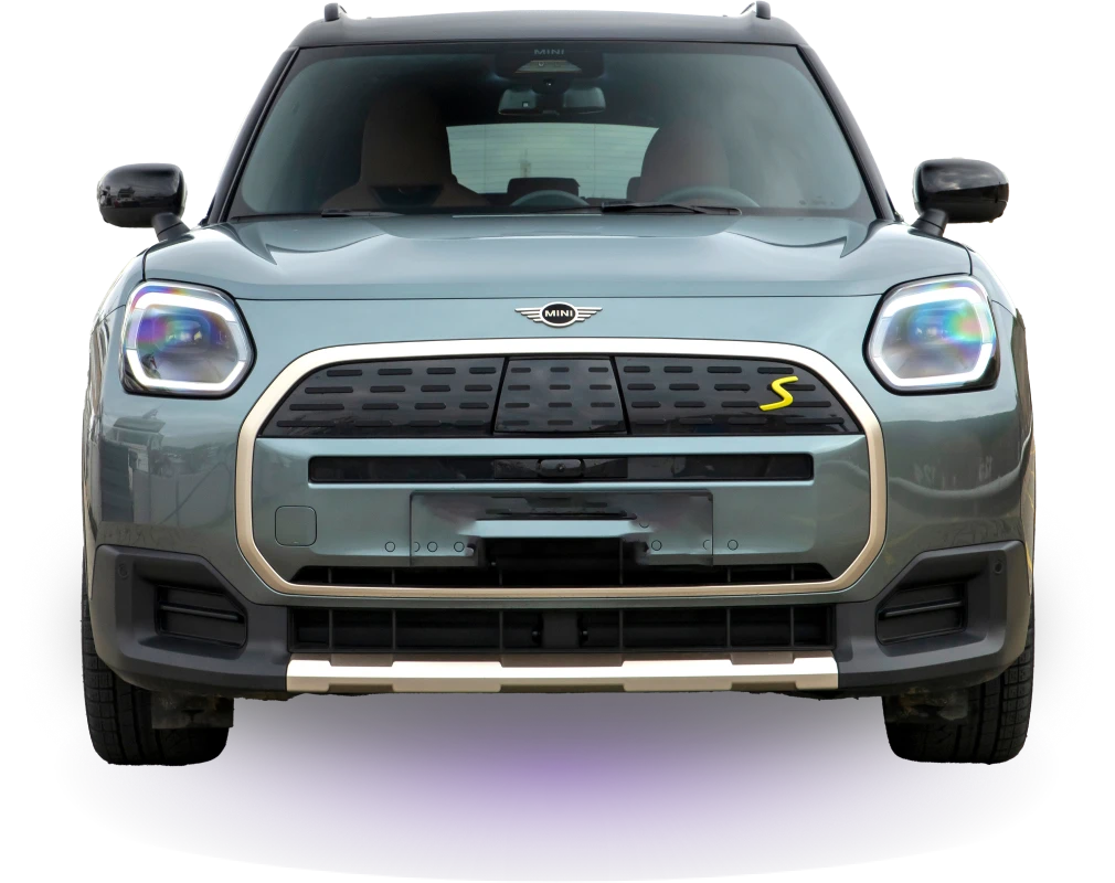 Front view of a green Mini Countryman SUV against a black background. The car features distinctive LED headlights and a sleek chrome grille.
